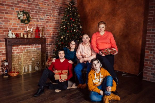 A family posing with Christmas gifts by a decorated tree indoors, exuding holiday warmth.