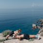 A couple performs a partner workout on a scenic cliffside, overlooking the ocean.